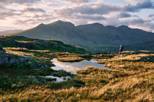 Female walker on Hard Knott looking towards Sca Fell at sunset. Lake District, Cumbria, UK.