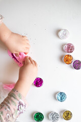 the hands of a little girl, a child who plays with plasticine and jars of sparkles. Child development, fine motor skills, hobbies, classes and home education. High quality photo