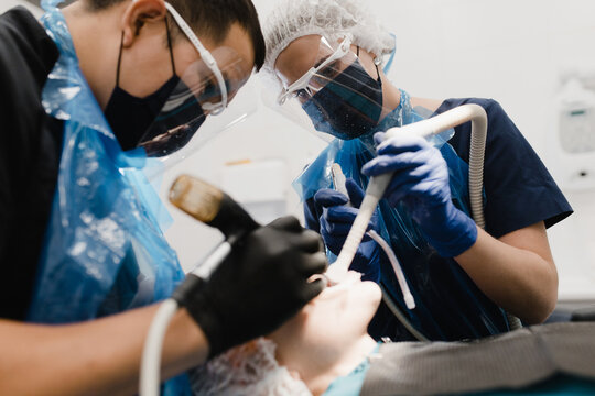 Female assistant with suction helping Asian dentist to heal patient