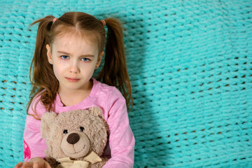 Little girl with cute pigtails is upset and crying. The child sits at home on a blue sofa and is very offended. Beautiful eyes fill with tears. Free space for text