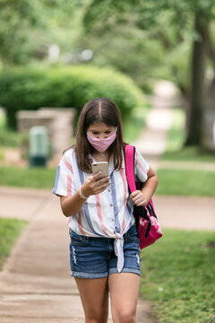 Student: Teen Girl With Face Mask Looks At Phone On Way To Schoo