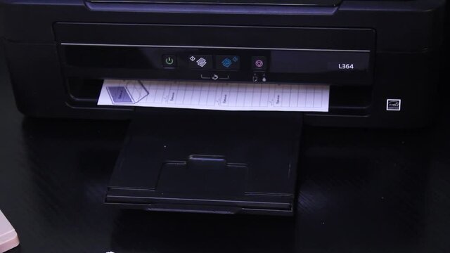 Printer In Action. Paper sheet being printed slowly from black printer