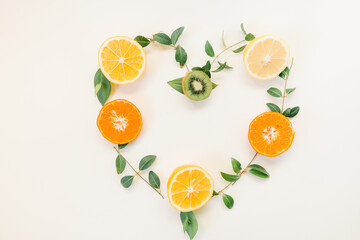 Creative summer healthy food  concept idea heart symbol border flame  made of citrus fruits lemon , orange and kiwi with  green leaves isolated on white background   . Flat lay, top view