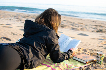 Joven mujer leyendo un libro al amanecer junto al mar. 