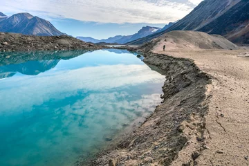 Foto op Canvas Hiker walking by a lake through remote arctic valley on a partly cloudy summer day. Dramatic arctic landscape of Akshayuk Pass, Baffin Island, Canada. Enormous glacier moraine. © Petr