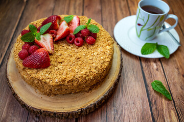 Homemade Napoleon cake (Mille-feuille) decorated with strawberries, raspberries and mint leaves on a wooden table.