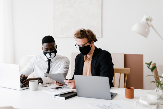 Multiethnic male colleagues in masks reading papers together