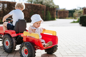 big brother and little sister sitting on a red toy tractor