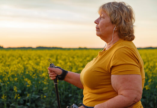 Chubby female walking with sticks against field and sundown sky