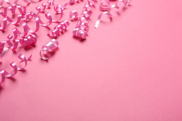 Shiny serpentine streamers on pink background, space for text