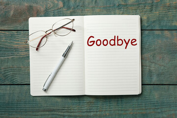 Notebook with word Goodbye on wooden table, top view