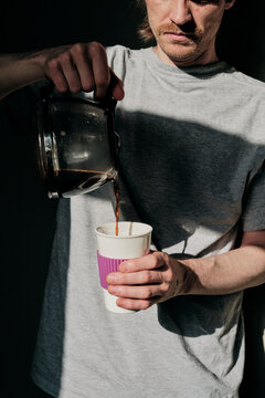 Young man pours coffee into a glass