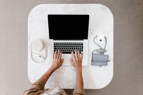 Crop senior woman using laptop near medical supplies