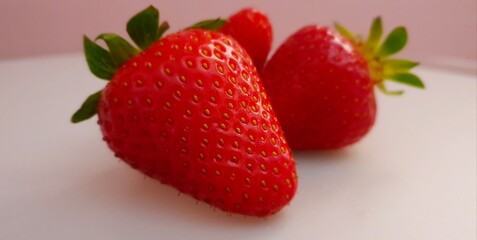 Fresh delicious strawberries lying on the table in front of pastel rose background