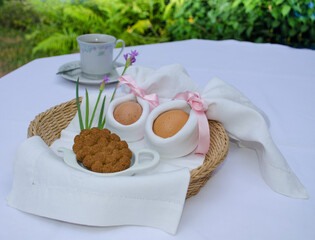 Beautiful festive Easter brunch with eggs in  napkin bunny, cup of tea, cookies and pink flowers on a basket. Easter outdoor celebration.
