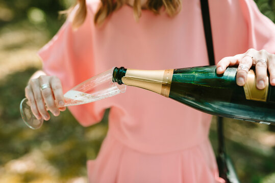 Girl With Pink Dress Pouring Champagne In A Plastic Glass