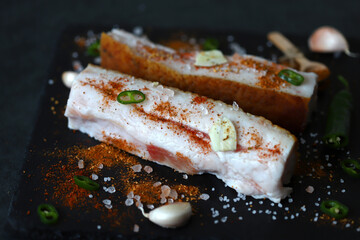 Spicy bacon on a stone board with spices. Salting lard.