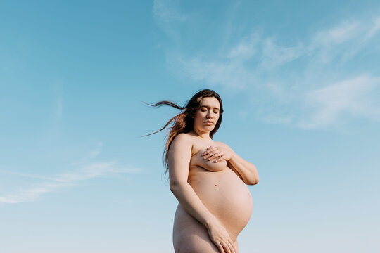 Naked pregnant woman against blue sky