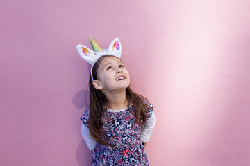 Adorable little girl wearing a unicorn headband with pink background