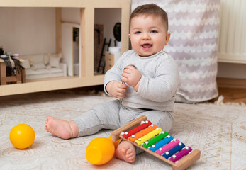 Cute funny baby boy play with colorful toys on the carpet in nursery room. Happy toddler child at home. Cheerful kid on the floor. Happy childhood. 