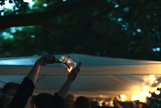 Putting on a candle in a glass jar hanging in a tree at dusk
