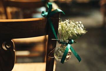 gypsophila flowers in a glass jar hanging with a green ribbon on a chair in church