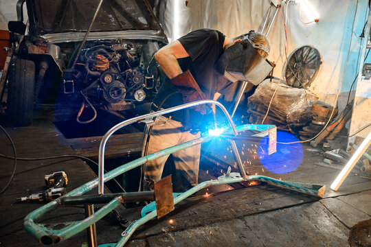 A man is engaged in welding work in a garage with a disassembled car