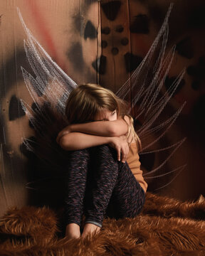 Child Sitting Alone with Art Wings on Wall