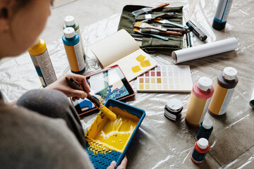 Unrecognizable woman taking yellow paint from tray on floor