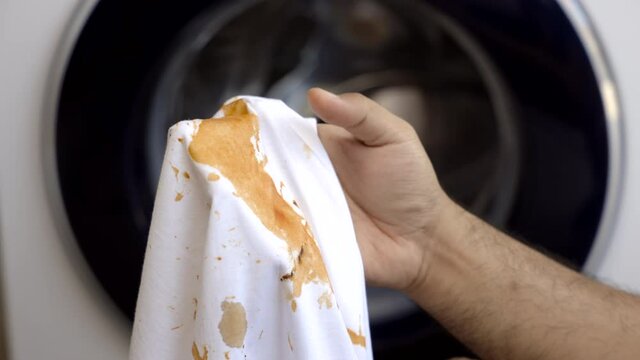 White cotton shirt So many stains and dirt. Stained ketchup The man's hand held the shirt and opened it to look at the dirt.