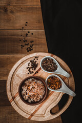 dry chili in ceramic bowl, accompanied by salt with chili pepper and pepper seeds, on a black cloth and a rustic dark background