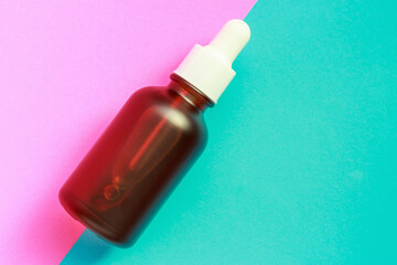 Bottle with serum on blue and pink background close-up, copy space.