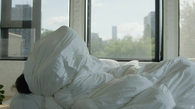 Young boy rolls off bed in bed sheets - slow motion