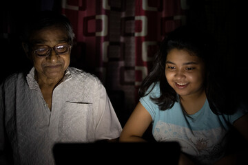 Teenage girl enjoying movie in laptop with grandfather