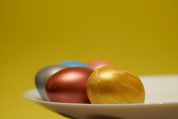 Painted eggs on a white plate with a yellow background.