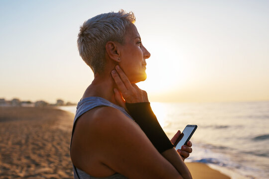 Mature jogger with smartphone checking pulse near sea