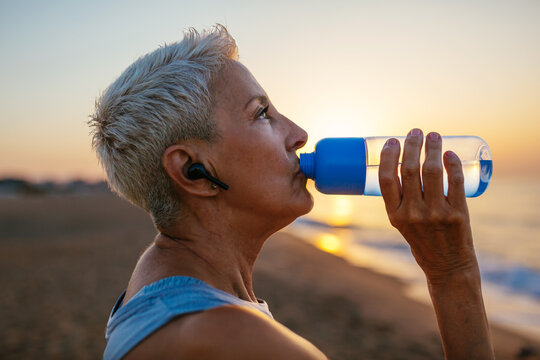 Middle aged athlete drinking water against sundown sky