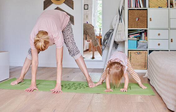 Mom and little daughter are doing yoga at home.