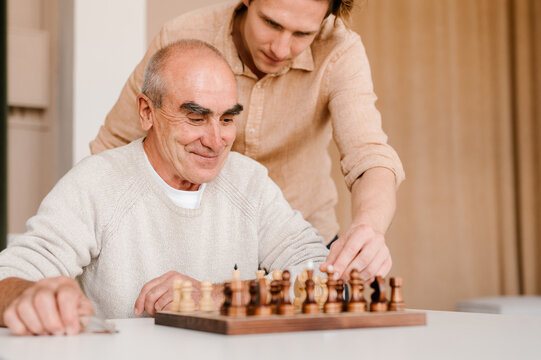 Happy senior man with son playing chess at home