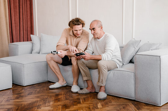 Young man teaching senior father to play video game