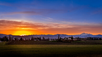 Blue and Orange Sky at Sunrise in the Fraser Valley of British Columbia, Canada with Mount Baker, a dormant volcano in Washington State, on the horizon