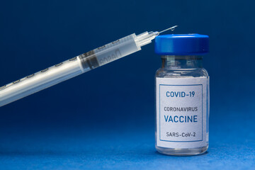 Vial of coronavirus Covid-19 vaccine and a syringe on a blue background.
