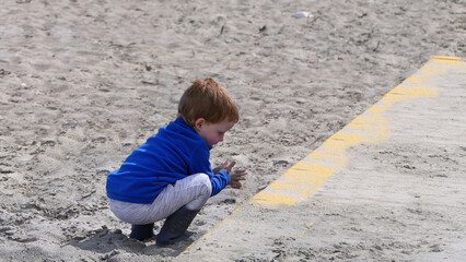 Red headed boy playing with Bucket spade and Digger on a sandy beach 