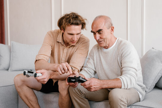 Young man teaching senior father to play video game