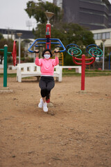 woman in pink polo shirt with chinstrap performs body weight exercises in public park. side shot. covid session