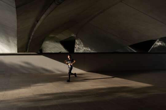 A young asian woman in running outdoors in the morning hours. First lights hits her as she runs under a bridge in the cities centre.