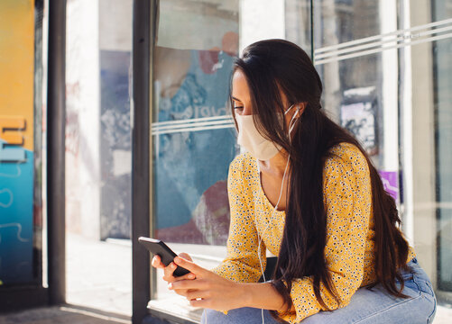 Young Woman sitting on the Bus Stop looking at her phone