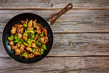 Spicy chicken teriyaki with broccoli in pan on wooden background.