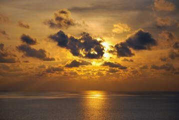 Obraz premium Sunset moment in the middle of the sea, with beautiful clouds covers some parts of the sun creating an amazing ray of light at the horizon. 