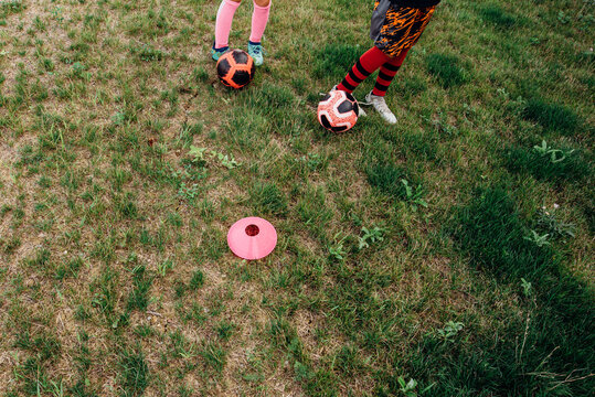 Siblings dribbling soccer ball between cones.